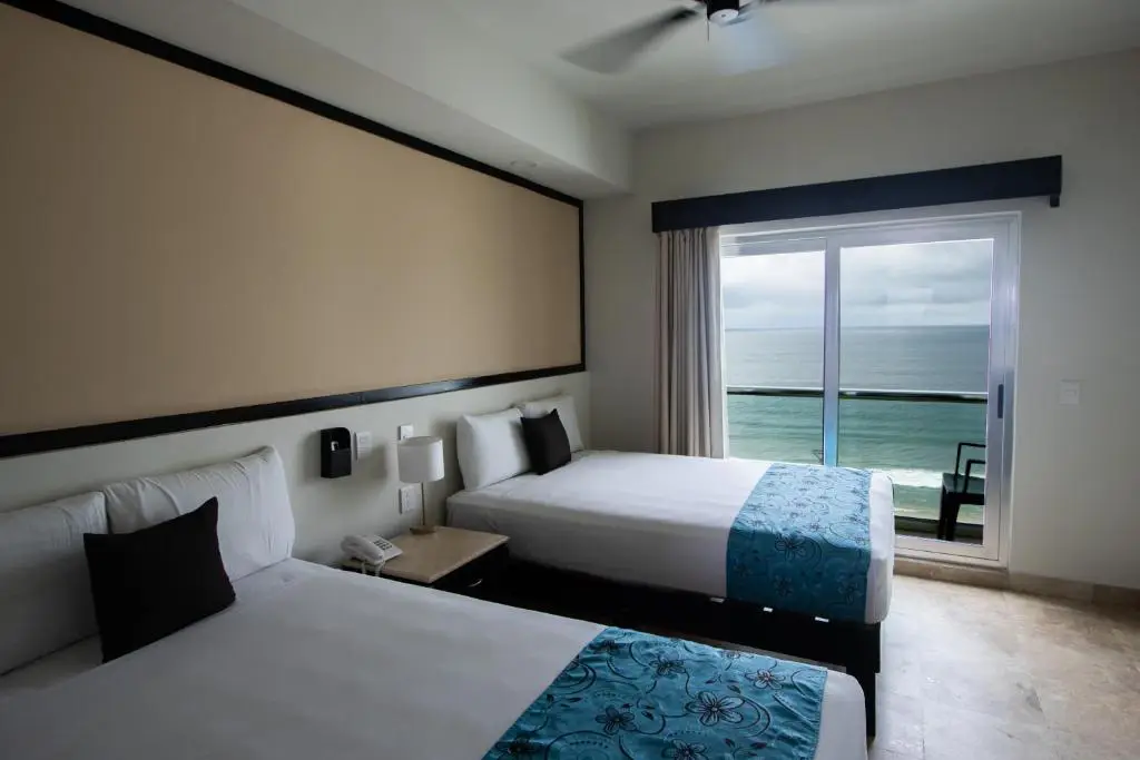 Habitación doble con camas separadas y balcón con vista al océano en hotel de Mazatlán, ideal para disfrutar comodidad y descanso con Royal Beach Paradise.